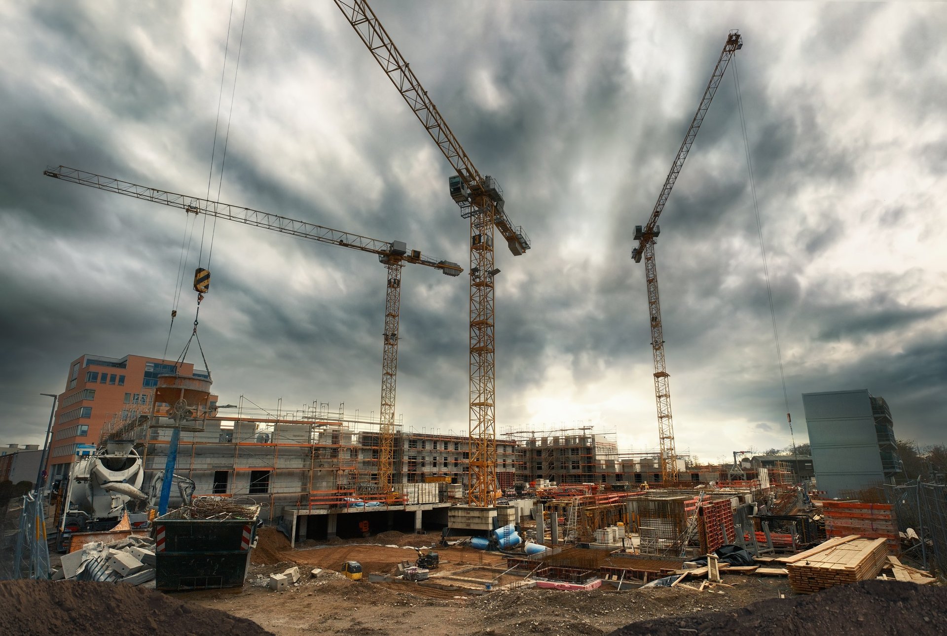 Construction site with cranes looming into the dramatic cloudy sky, wide angle view