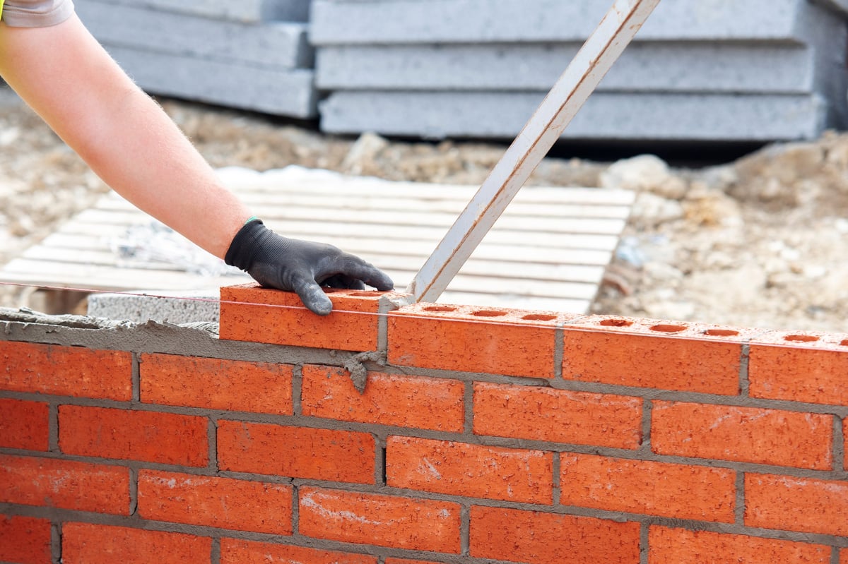 Close-up of skilled bricklayer working on construction site laying red bricks for wall construction