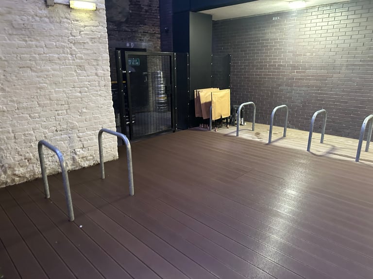 Empty studio or gym space with wooden flooring, white metal benches along the walls, exposed brick, and industrial lighting