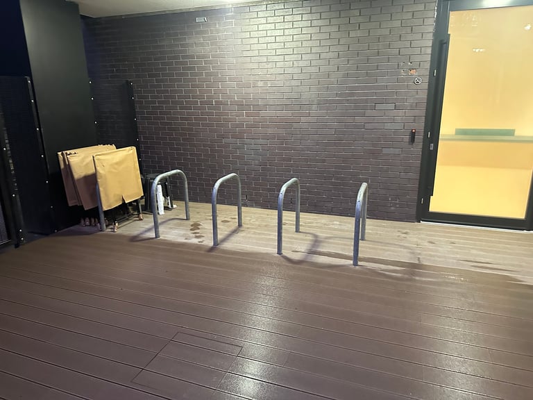 Empty indoor parking area with four bicycle racks against a dark brick wall and wooden flooring